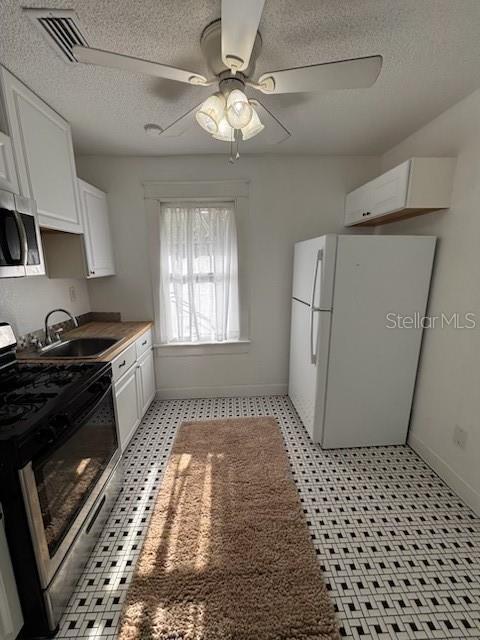 kitchen featuring stainless steel appliances, a textured ceiling, white cabinetry, and a sink