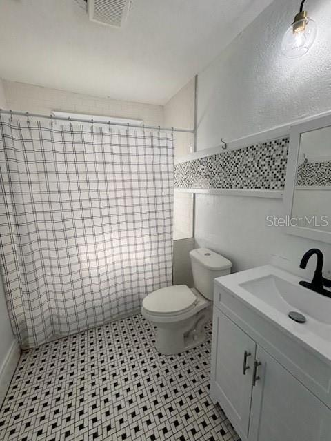 full bath with vanity, toilet, tile walls, a shower with curtain, and visible vents