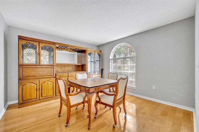 dining space with baseboards, a textured ceiling, and light wood-style flooring