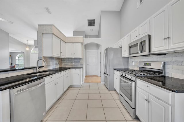 kitchen with a sink, stainless steel appliances, decorative backsplash, arched walkways, and white cabinets