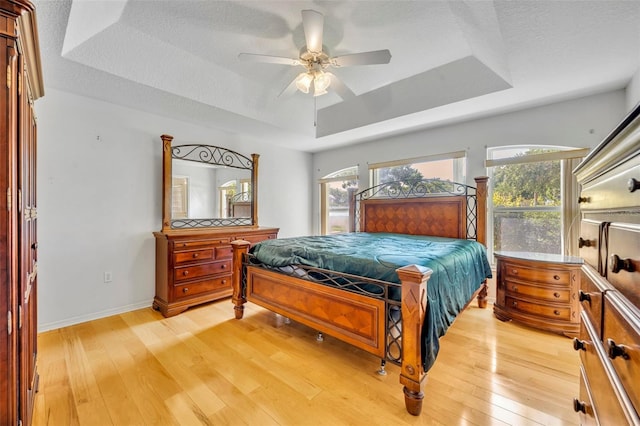 bedroom featuring a raised ceiling, light wood-style flooring, and multiple windows