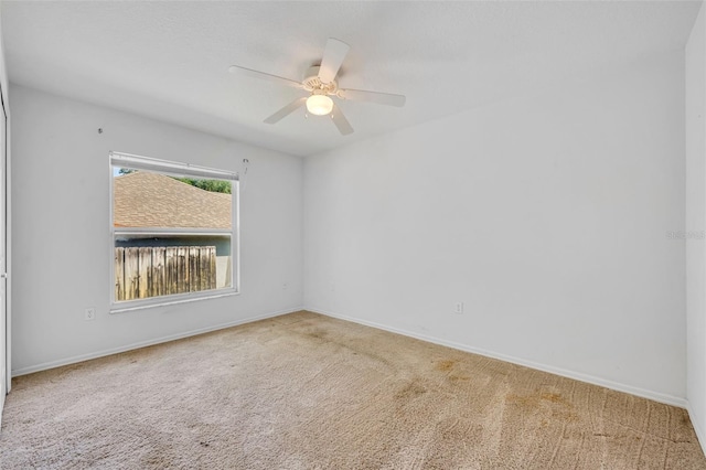 carpeted empty room featuring a ceiling fan and baseboards