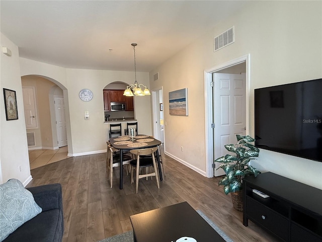 dining area featuring dark wood finished floors, arched walkways, a chandelier, baseboards, and visible vents