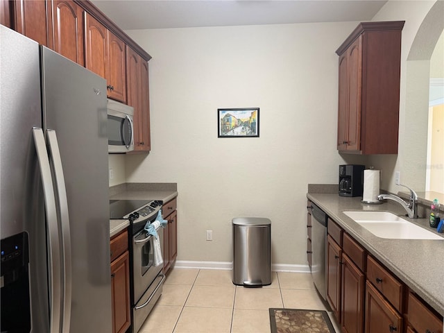 kitchen with arched walkways, light tile patterned floors, stainless steel appliances, a sink, and baseboards
