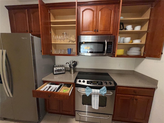 kitchen featuring appliances with stainless steel finishes, light tile patterned flooring, brown cabinets, and open shelves
