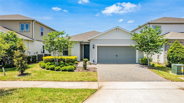 view of front of house featuring decorative driveway, stucco siding, central AC unit, a front lawn, and a garage
