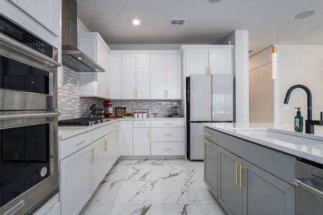 kitchen with light countertops, appliances with stainless steel finishes, wall chimney range hood, and a sink