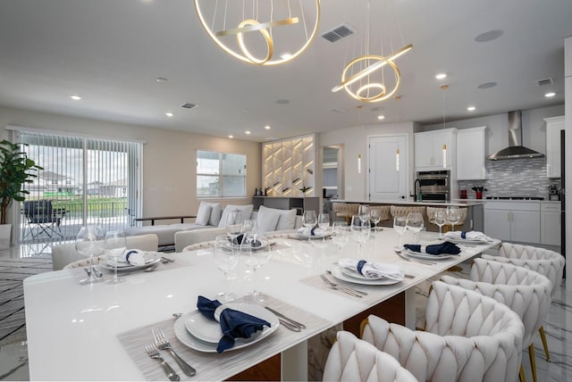 kitchen featuring wall chimney range hood, visible vents, open floor plan, stainless steel double oven, and a notable chandelier