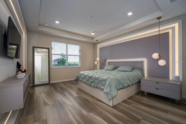 bedroom with recessed lighting, baseboards, wood finished floors, and a tray ceiling