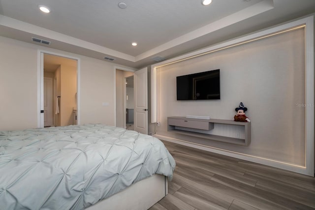 bedroom with wood finished floors, visible vents, recessed lighting, and a tray ceiling