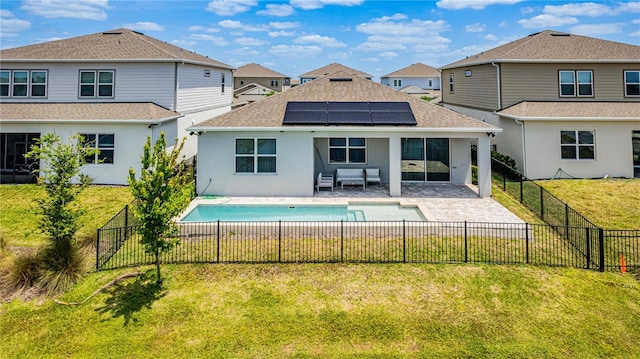 rear view of house with stucco siding, a yard, a fenced in pool, a patio, and solar panels