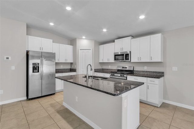 kitchen with appliances with stainless steel finishes, a sink, light tile patterned floors, white cabinets, and dark stone countertops