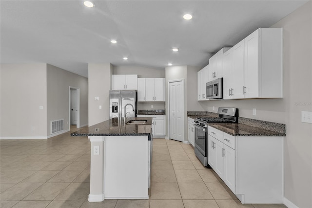 kitchen featuring a sink, an island with sink, dark stone countertops, stainless steel appliances, and light tile patterned floors