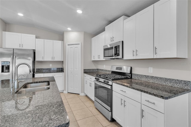 kitchen featuring white cabinets, appliances with stainless steel finishes, a sink, and dark stone countertops