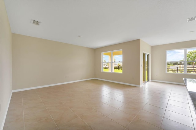 empty room featuring light tile patterned flooring, visible vents, baseboards, and a healthy amount of sunlight