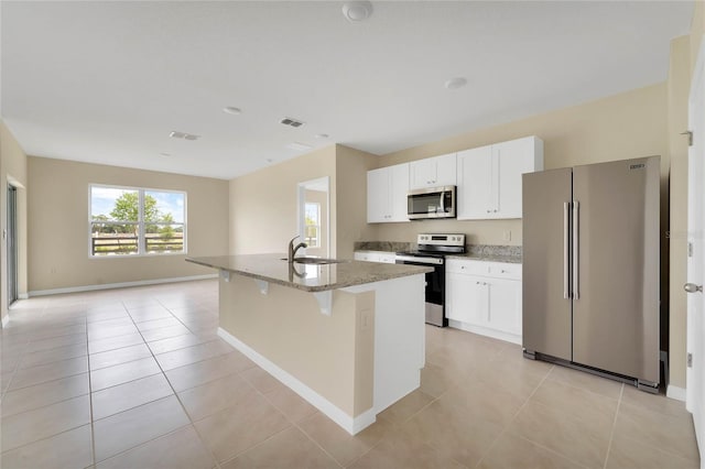 kitchen with a kitchen island with sink, light stone countertops, a sink, stainless steel appliances, and white cabinetry