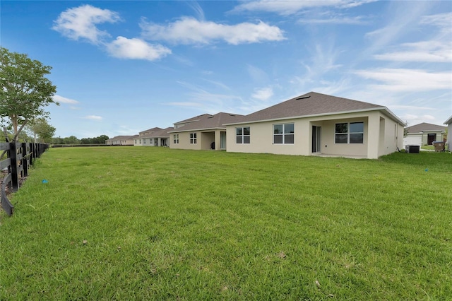 back of property featuring stucco siding, fence, roof with shingles, central AC, and a lawn