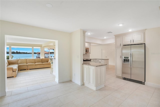 kitchen featuring baseboards, light stone counters, a peninsula, a water view, and stainless steel appliances