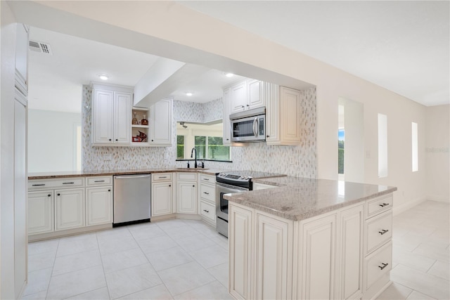 kitchen with open shelves, appliances with stainless steel finishes, a peninsula, a wealth of natural light, and tasteful backsplash