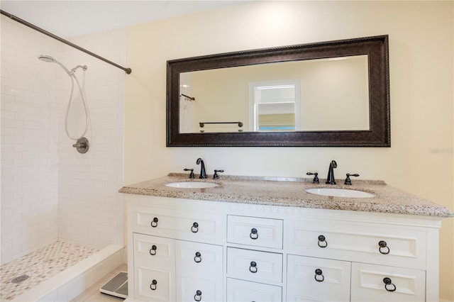 bathroom featuring double vanity, a tile shower, and a sink