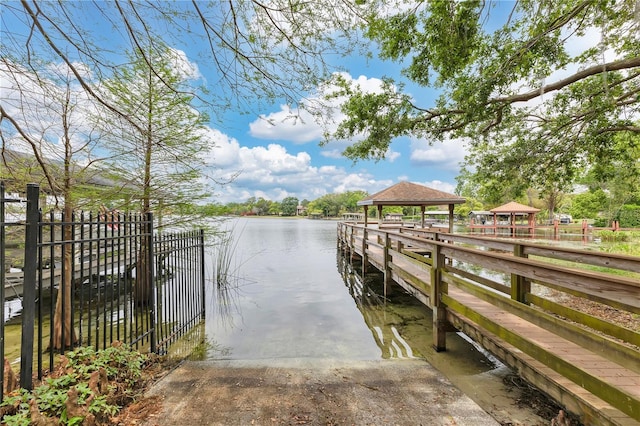 dock area with a gazebo, a water view, and fence