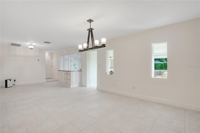 unfurnished room with baseboards, a wealth of natural light, and a notable chandelier