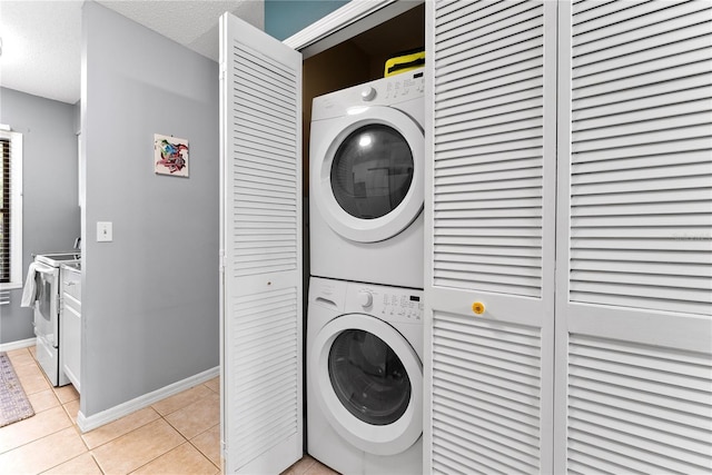 laundry room featuring stacked washer and clothes dryer, light tile patterned floors, baseboards, and a textured ceiling