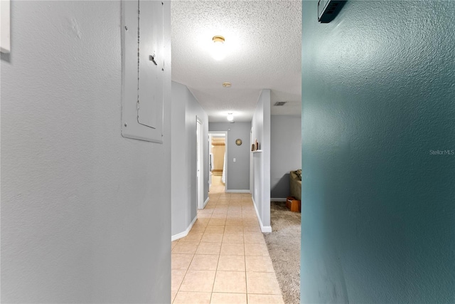 hall featuring light tile patterned floors, baseboards, and a textured ceiling