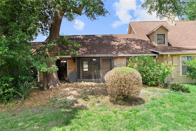 rear view of property featuring roof with shingles, a yard, a sunroom, and a chimney