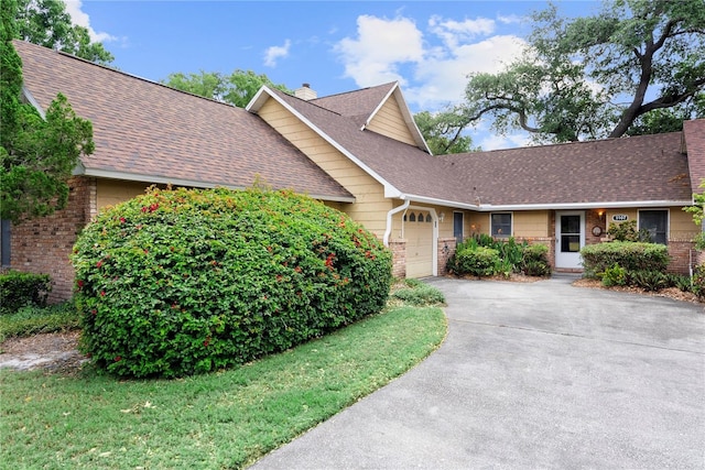 view of front of property with a garage, a shingled roof, concrete driveway, brick siding, and a chimney