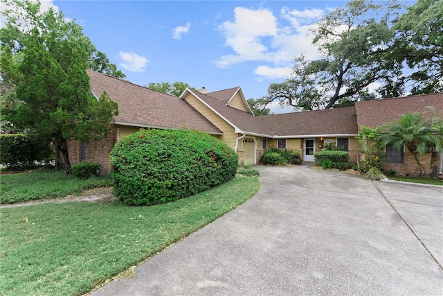 view of front facade featuring driveway, brick siding, an attached garage, a front yard, and roof with shingles