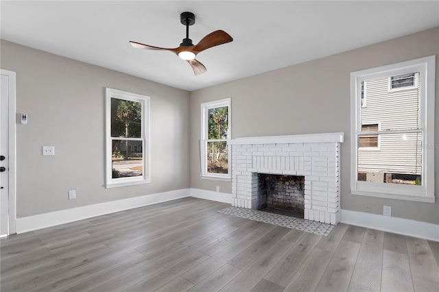 unfurnished living room featuring baseboards, a brick fireplace, ceiling fan, and wood finished floors