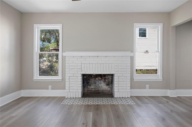 unfurnished living room with baseboards, a brick fireplace, and wood finished floors