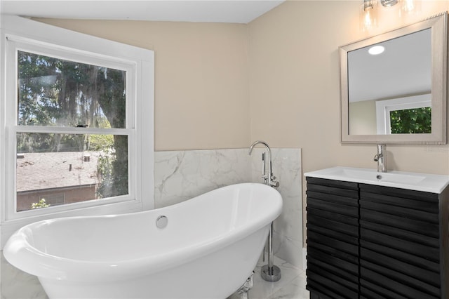 bathroom featuring vanity, marble finish floor, wainscoting, a freestanding tub, and tile walls