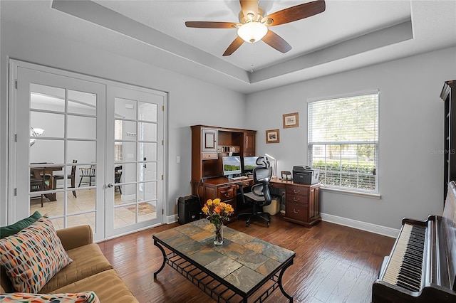 home office featuring a ceiling fan, a tray ceiling, baseboards, and hardwood / wood-style flooring