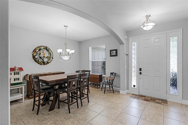dining room with baseboards, a textured ceiling, a chandelier, arched walkways, and light tile patterned floors