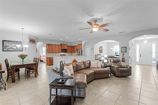 living area featuring arched walkways, visible vents, light tile patterned floors, and ceiling fan with notable chandelier