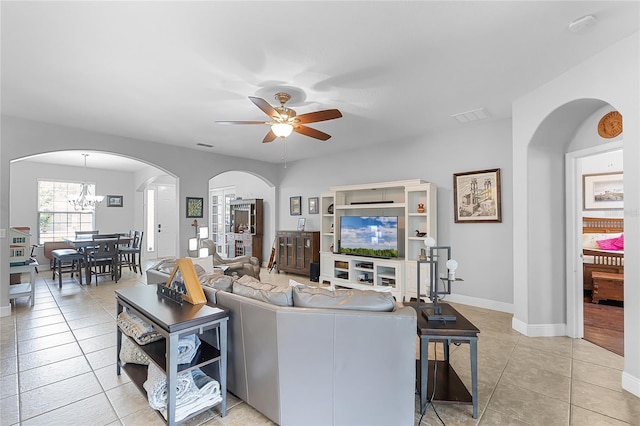 living room featuring visible vents, arched walkways, light tile patterned floors, baseboards, and ceiling fan with notable chandelier