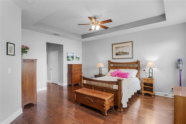 bedroom featuring visible vents, hardwood / wood-style floors, baseboards, a tray ceiling, and a ceiling fan