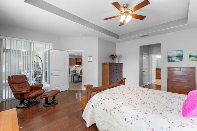 bedroom featuring ceiling fan, a tray ceiling, wood finished floors, and visible vents