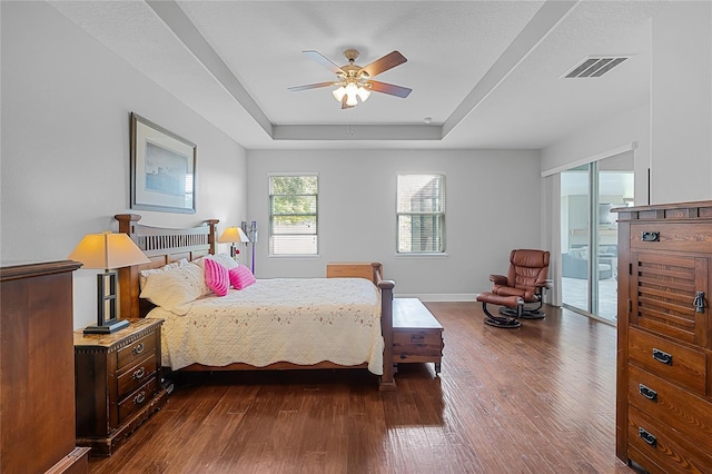 bedroom with visible vents, baseboards, dark wood-type flooring, and a tray ceiling