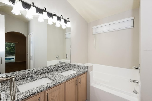 bathroom with double vanity, a bath, lofted ceiling, and a sink