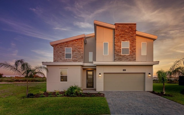contemporary home with an attached garage, stucco siding, a lawn, and stone siding