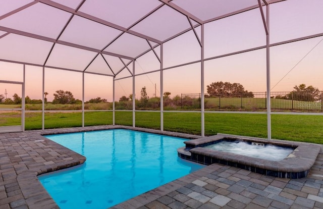 pool at dusk with a pool with connected hot tub, a patio, glass enclosure, and a lawn