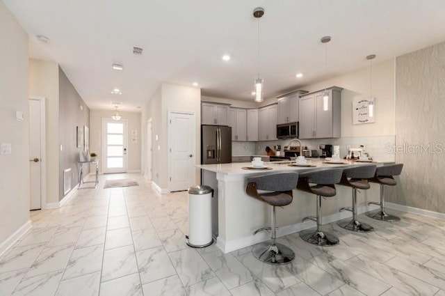 kitchen featuring a peninsula, marble finish floor, gray cabinets, a breakfast bar area, and appliances with stainless steel finishes