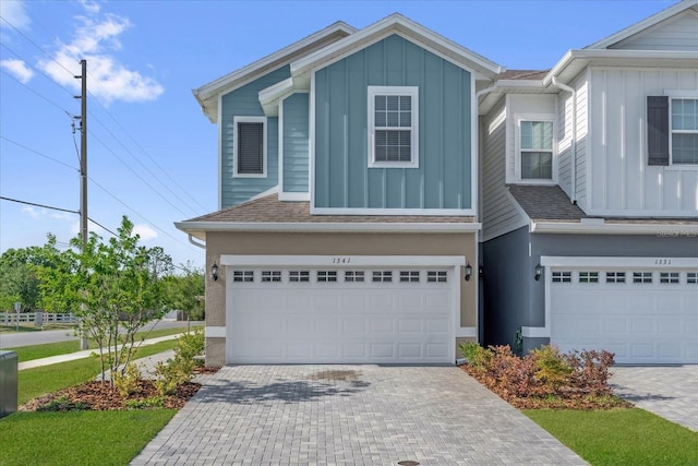multi unit property with a garage, board and batten siding, a shingled roof, and decorative driveway