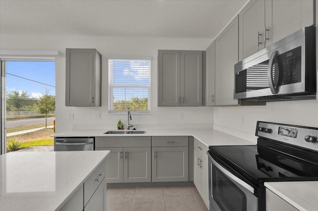 kitchen featuring a sink, gray cabinetry, stainless steel appliances, light tile patterned flooring, and light stone countertops