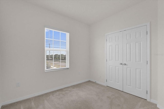 unfurnished bedroom featuring a closet, light colored carpet, and baseboards