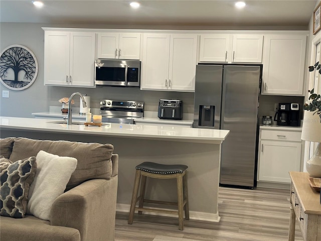 2000 Golden Beak Dr, Eagle Lake, FL 33839 - kitchen featuring a sink, light wood-style floors, a kitchen breakfast bar, stainless steel appliances, and white cabinetry