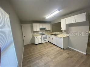 kitchen featuring white range with electric stovetop, wood finished floors, light countertops, and white cabinetry